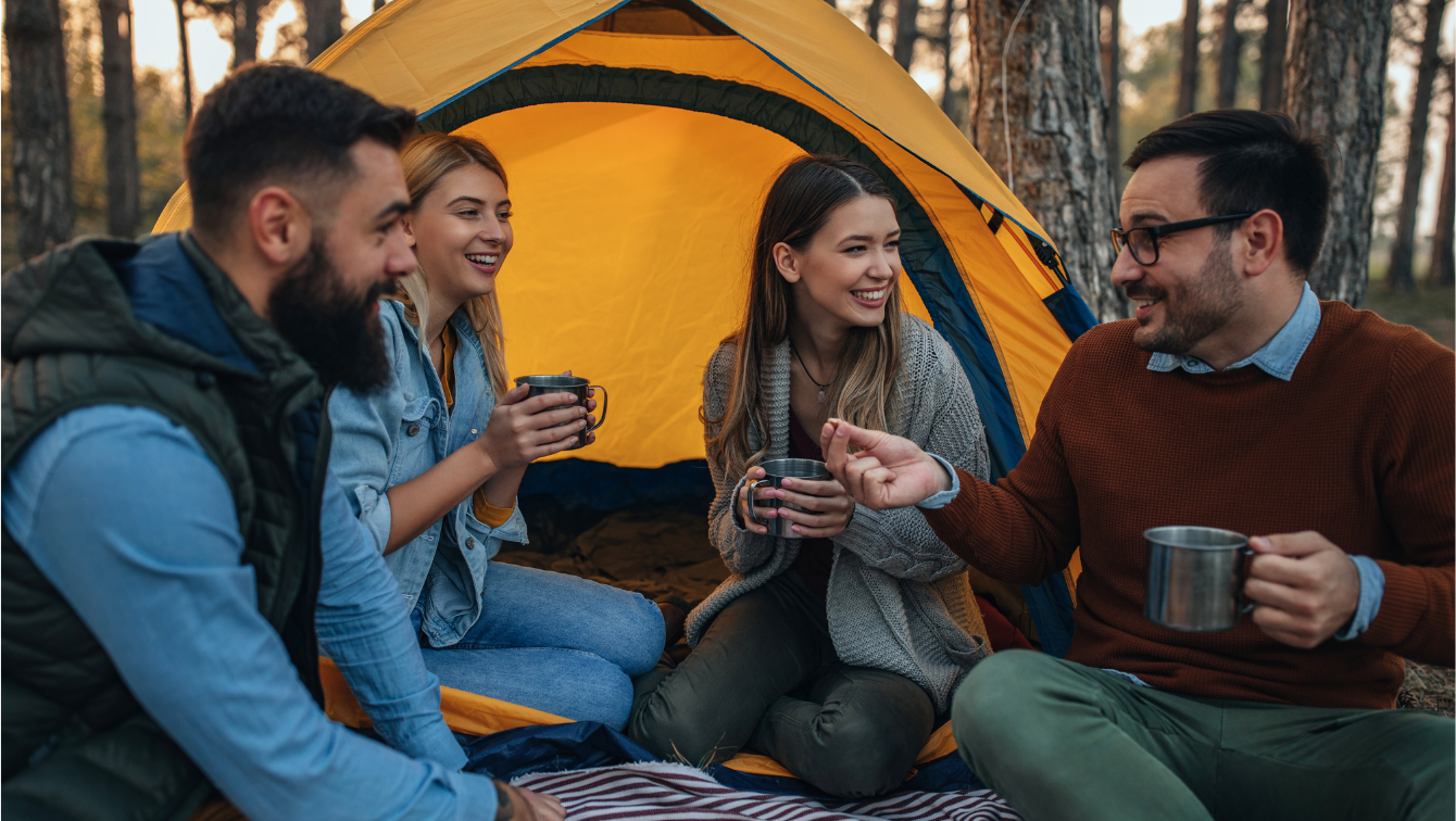 Four friends are sitting next to a tent, having a lively conversation while sipping out of their metal mugs