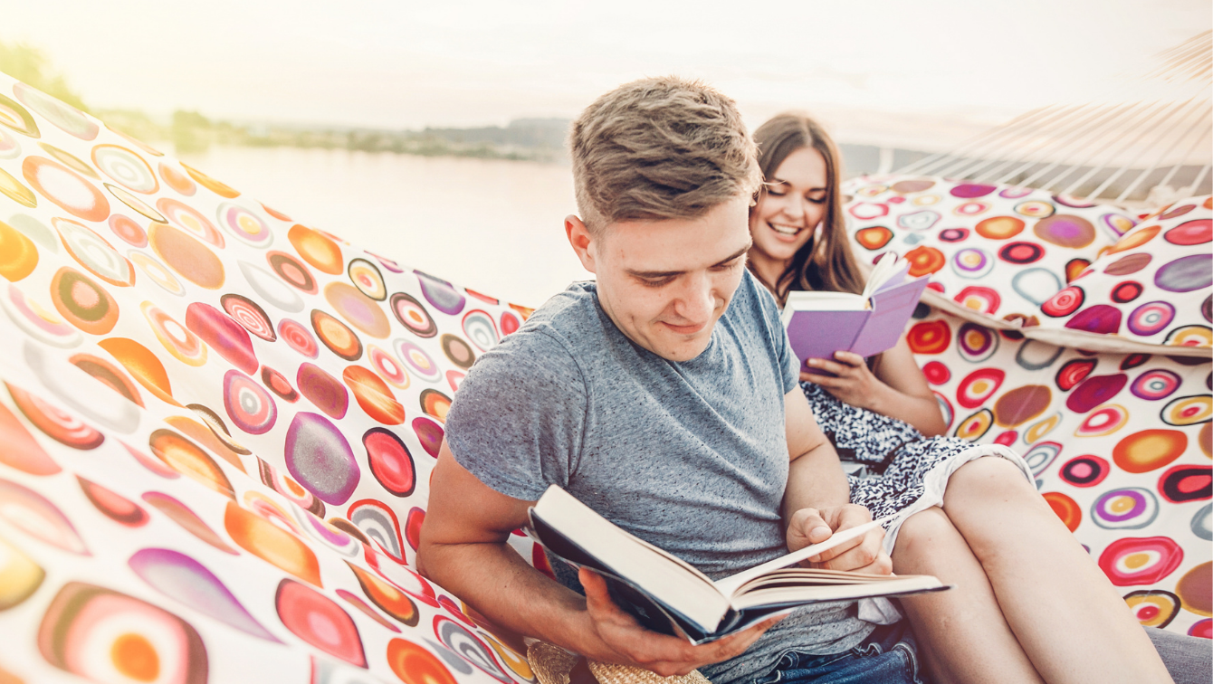 Two people are sharing a hammock on a sunny day while reading their books