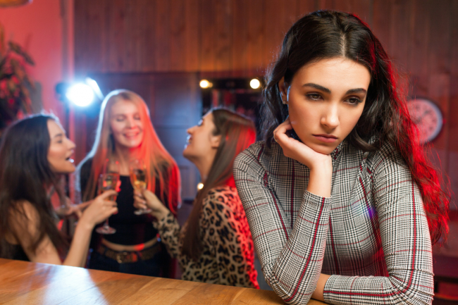 Sad person in a bar with happy people partying at the background. 