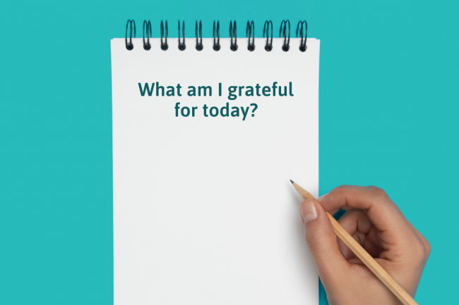 A notepad with the title "What am I grateful for today?" and a hand holding a pencil. 