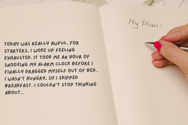 A journal notebook in perspective with a hand holding a pencil and writing "My plans" on it.