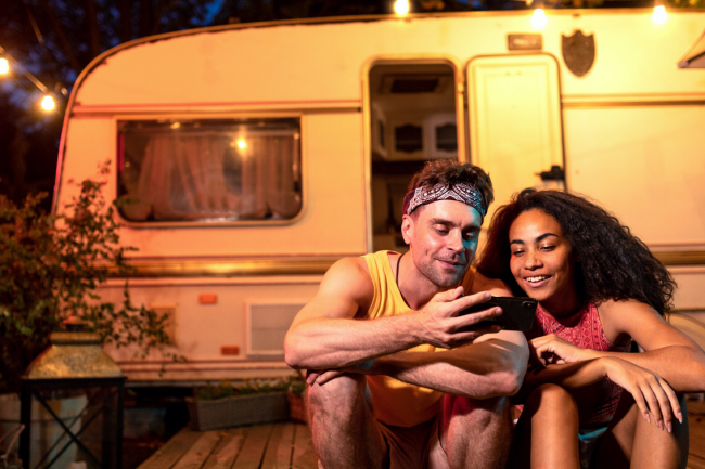 Two friends at night look at the phone together in front of a trailer. 