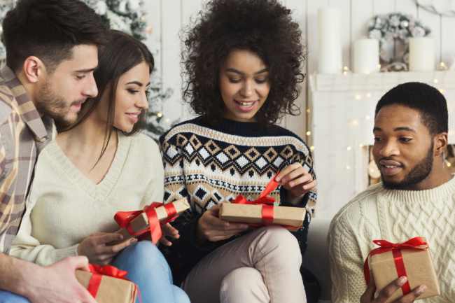 Four friends exchange gifts, everyone is looking when one of them is opening their gift.