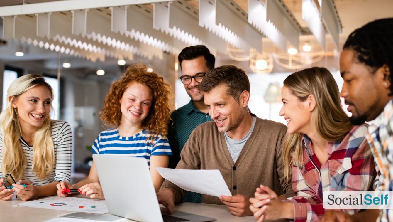 Several coworkers smile while one of them is showing them something on his laptop.