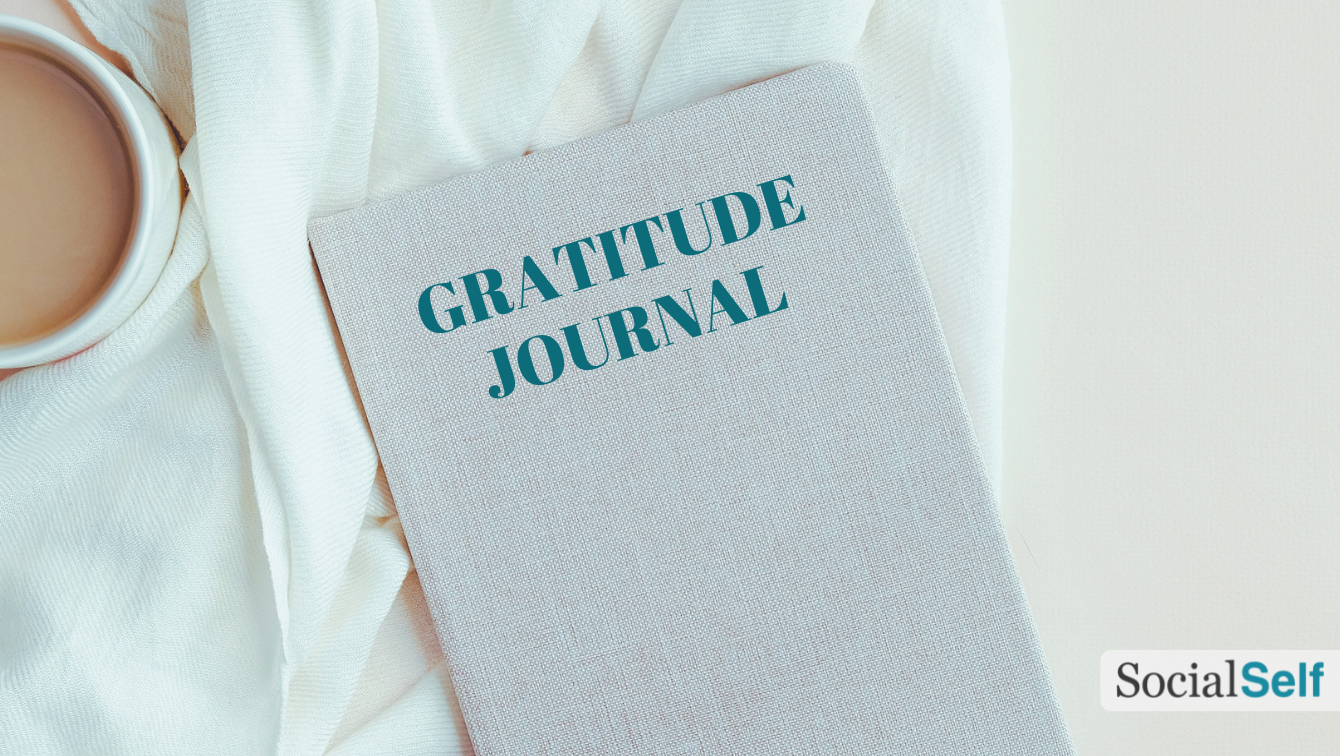A gratitude journal on a table, and near a cup of coffee seen from above. 