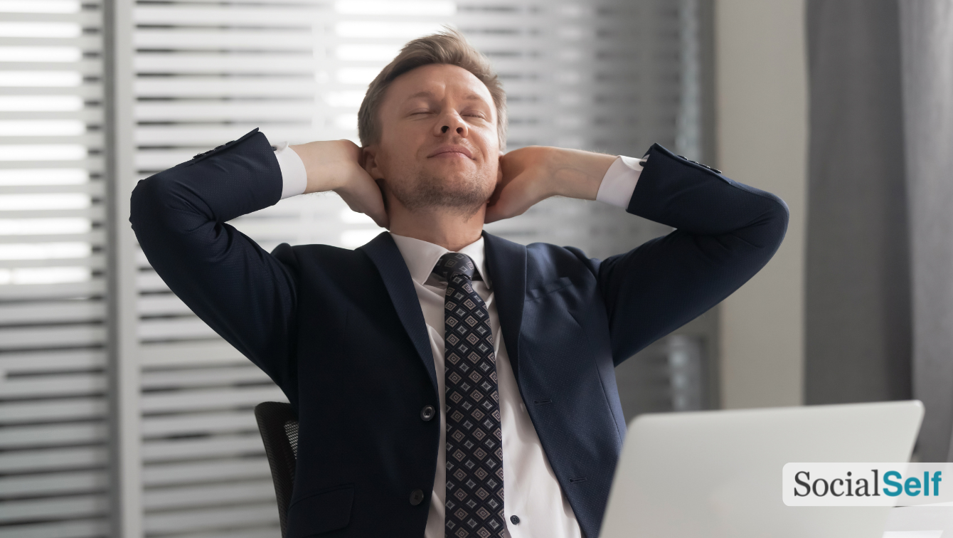 A worker in a suit relaxing at the office with their hands behind their neck and stretching their spine